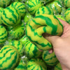 A hand holds a bright green watermelon squishy stress ball with a striped texture.