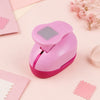A pink decorative square stamp edge paper punch is shown on a light pink surface with other paper items.