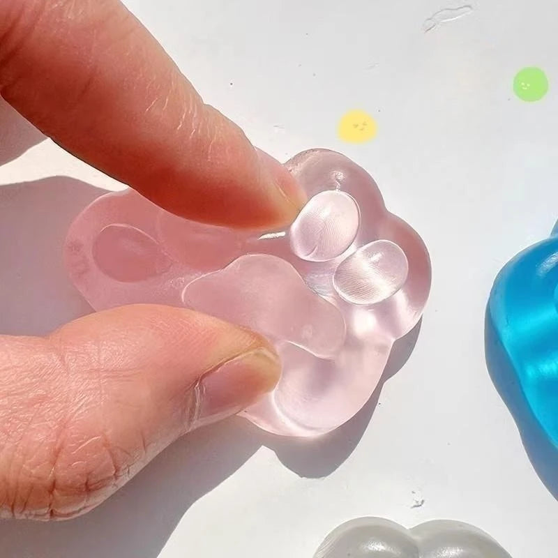 A hand is squeezing a translucent pink jelly cat paw squishy toy against a white background.