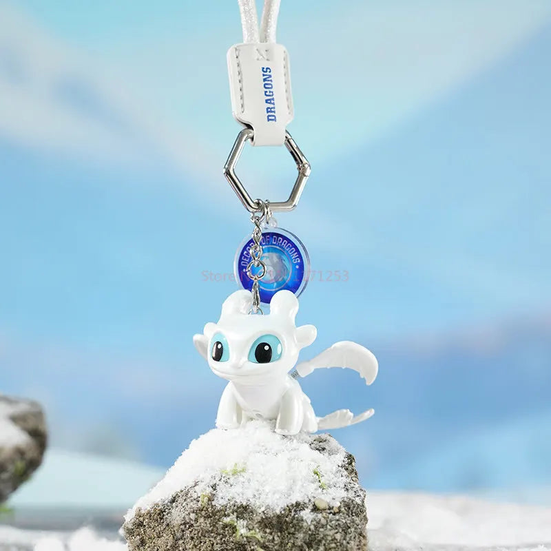 A white Toothless Dragon keychain with movable wings and glowing eyes resting on a snowy rock.