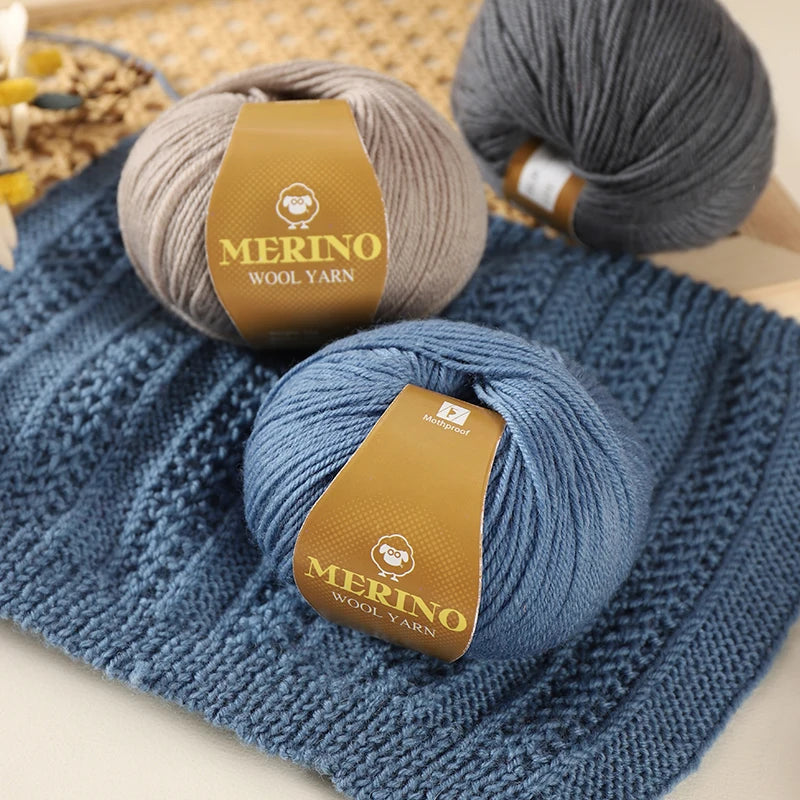 A ball of Merino wool yarn in a light gray color resting on a blue knitted fabric.