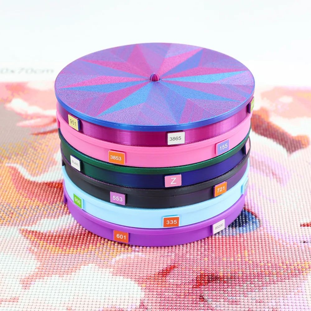 A stack of colorful rotating diamond painting storage trays with various numbered lids on a pink and white patterned surface.