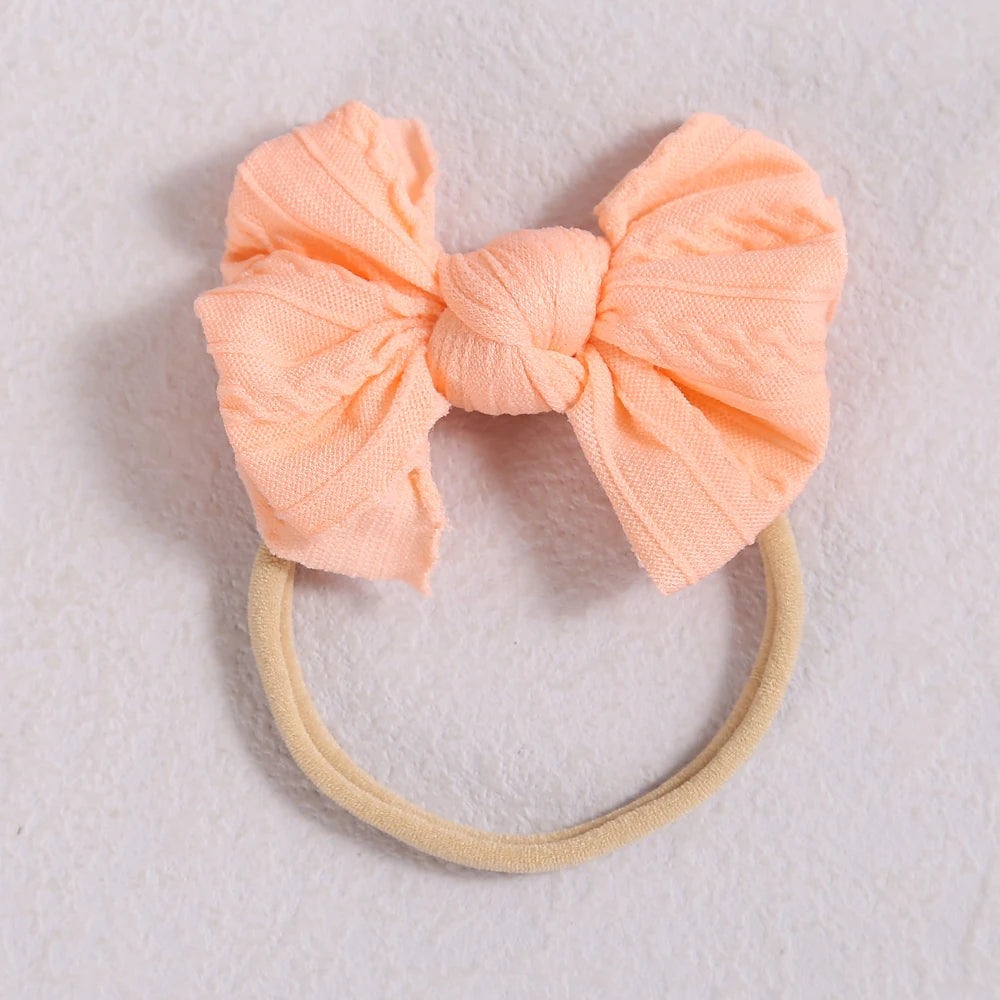 A soft peach colored fabric bow headband with a light beige elastic band.
