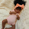 A lifelike 19-inch reborn baby doll with hand-rooted black hair lying on a fluffy white surface.