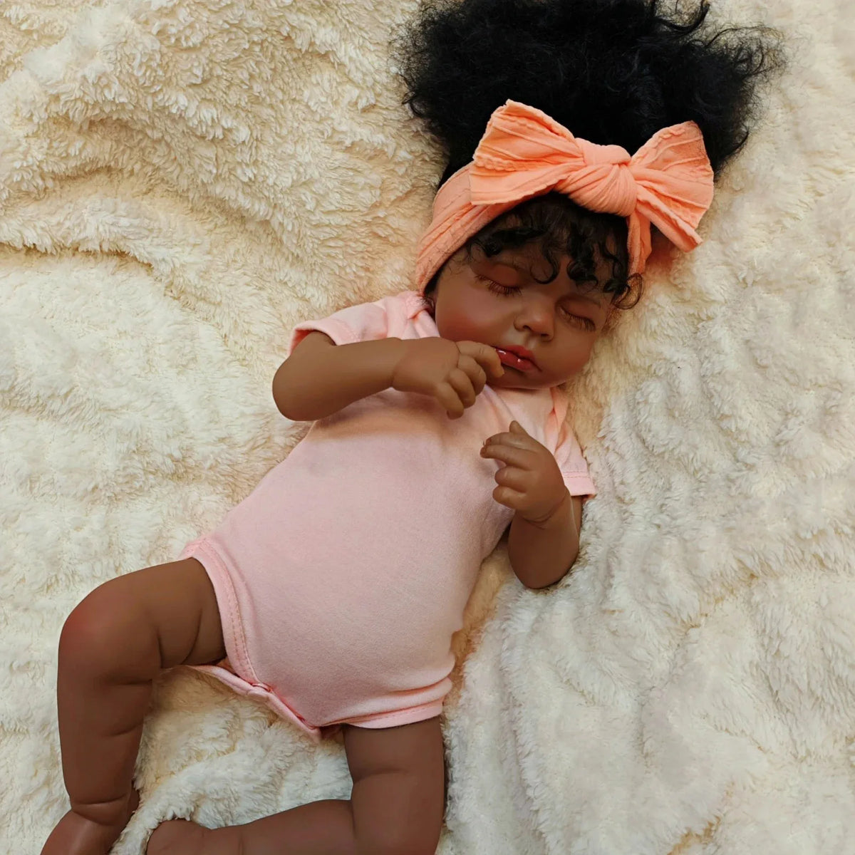 A lifelike 19-inch reborn baby doll with hand-rooted black hair lying on a fluffy white surface.