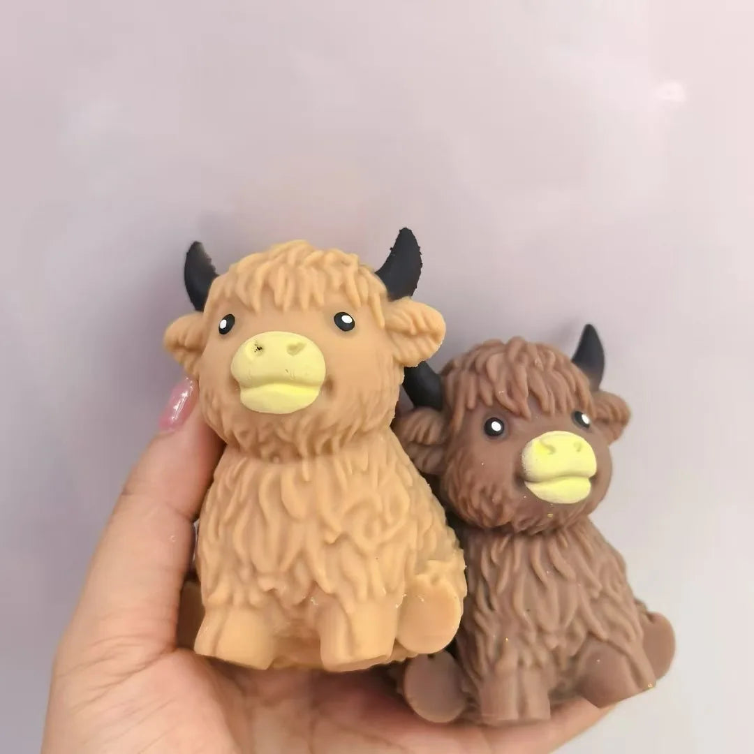 A hand holds a brown Scottish Highland cow stress relief squishy toy.