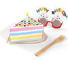 A colorful layer cake with a candle, surrounded by party decorations and a wooden fork.