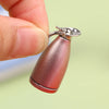 A small, rose gold-colored miniature alloy kettle with a silver handle is held by a person's fingers.