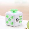 A white fidget cube with green buttons and a rotating joystick is shown on a light wooden surface.