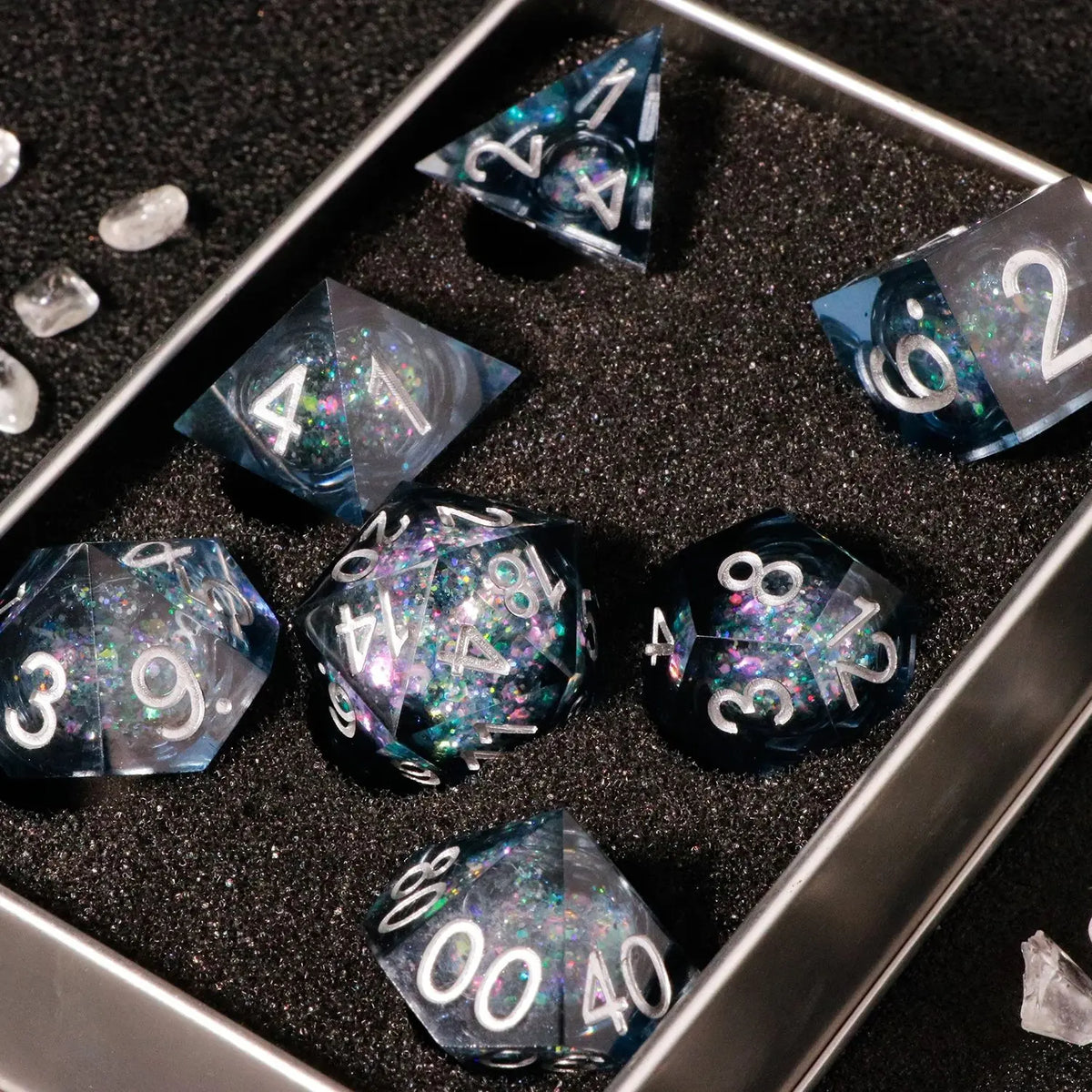A set of handmade liquid core polyhedral dice with a galaxy finish displayed in a metal tray.