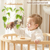A baby is interacting with a wooden felt forest animal bed bell mobile featuring giraffe and monkey figures.