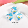 Three clear resin charms shaped like blue fish with pink accents displayed on a white plate.
