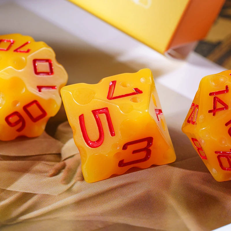 A close-up of yellow cheese-themed polyhedral dice set with red numbers resting on brown paper.