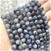 A close-up of small, round, deep blue to purple natural stone beads being held in a hand.
