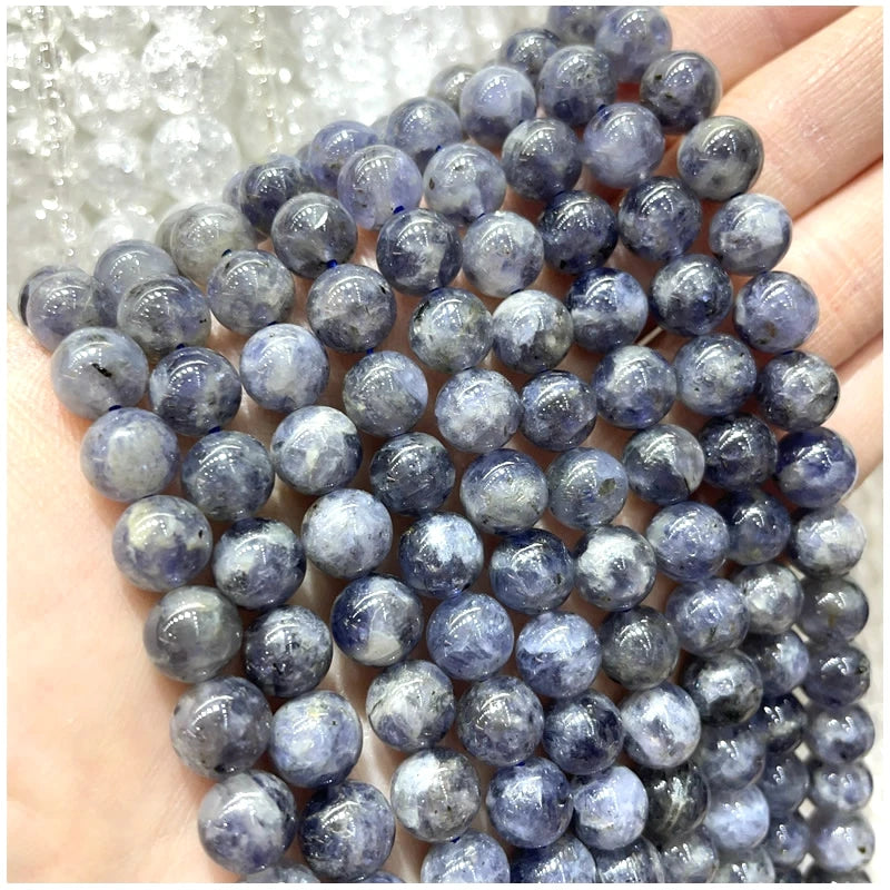A close-up of small, round, deep blue to purple natural stone beads being held in a hand.