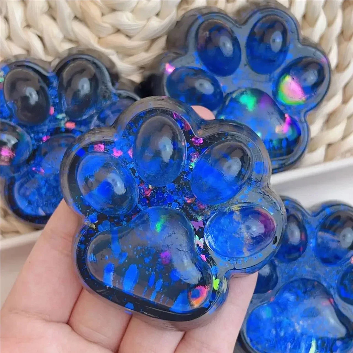 A hand holds a blue translucent silicone paw print fidget toy with iridescent glitter.