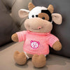 A soft pink plush cow stuffed animal with black and white markings sitting on a neutral surface.