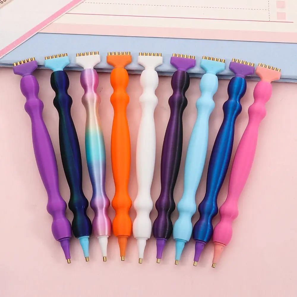 A row of precision diamond painting pens in various colors including purple, blue, orange, and pink.