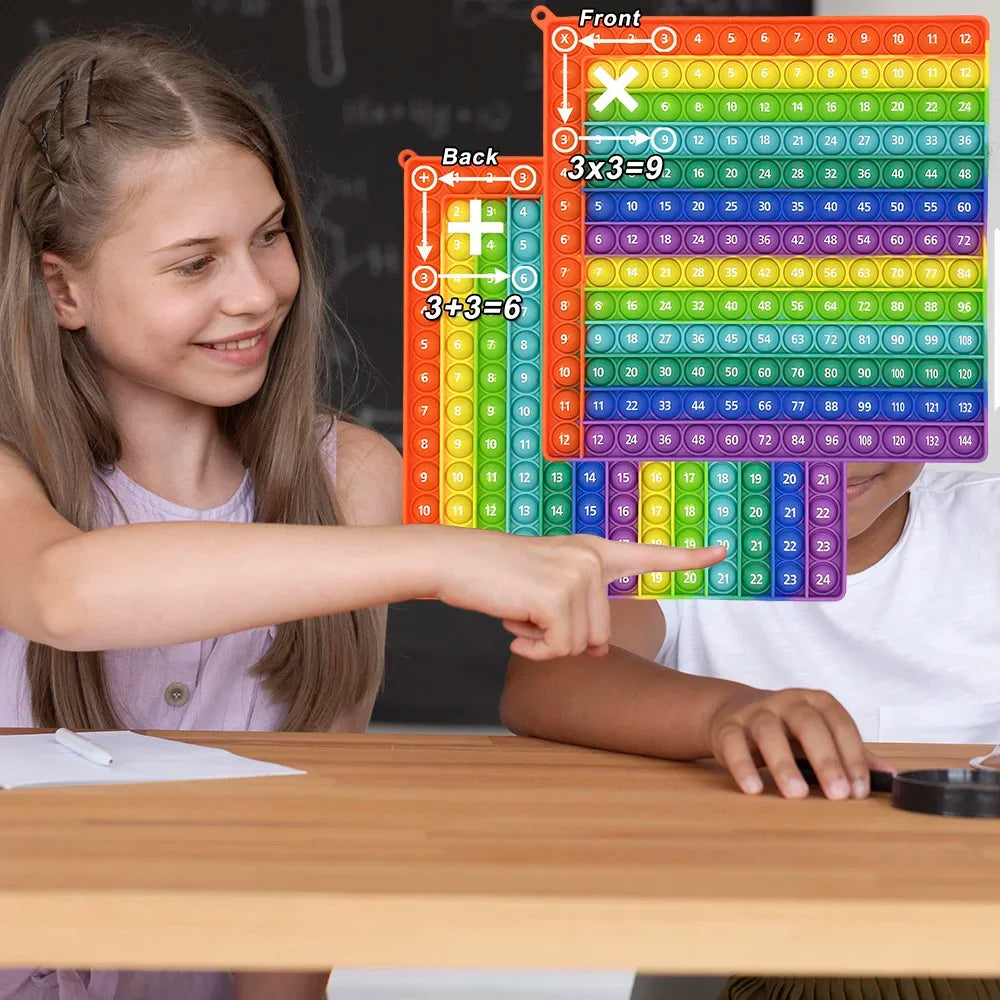A girl points to a colorful grid of multiplication and addition fidget toys on a wooden table.