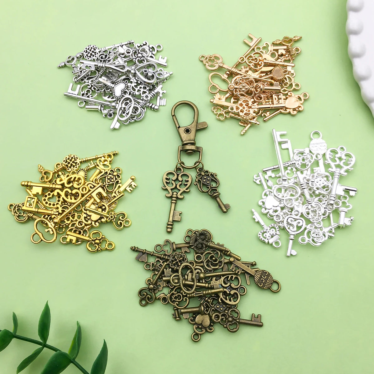 A collection of vintage brass and silver key charms and pendants for jewelry making displayed on a light green surface.