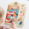 A toddler is interacting with a wooden Tetris-style geometric shape puzzle featuring colorful blocks.