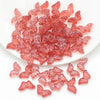 A pile of pink and reddish glass butterfly beads for jewelry making