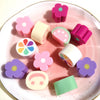 A collection of pink and purple polymer clay marshmallow charms in various shapes arranged on a light pink plate.