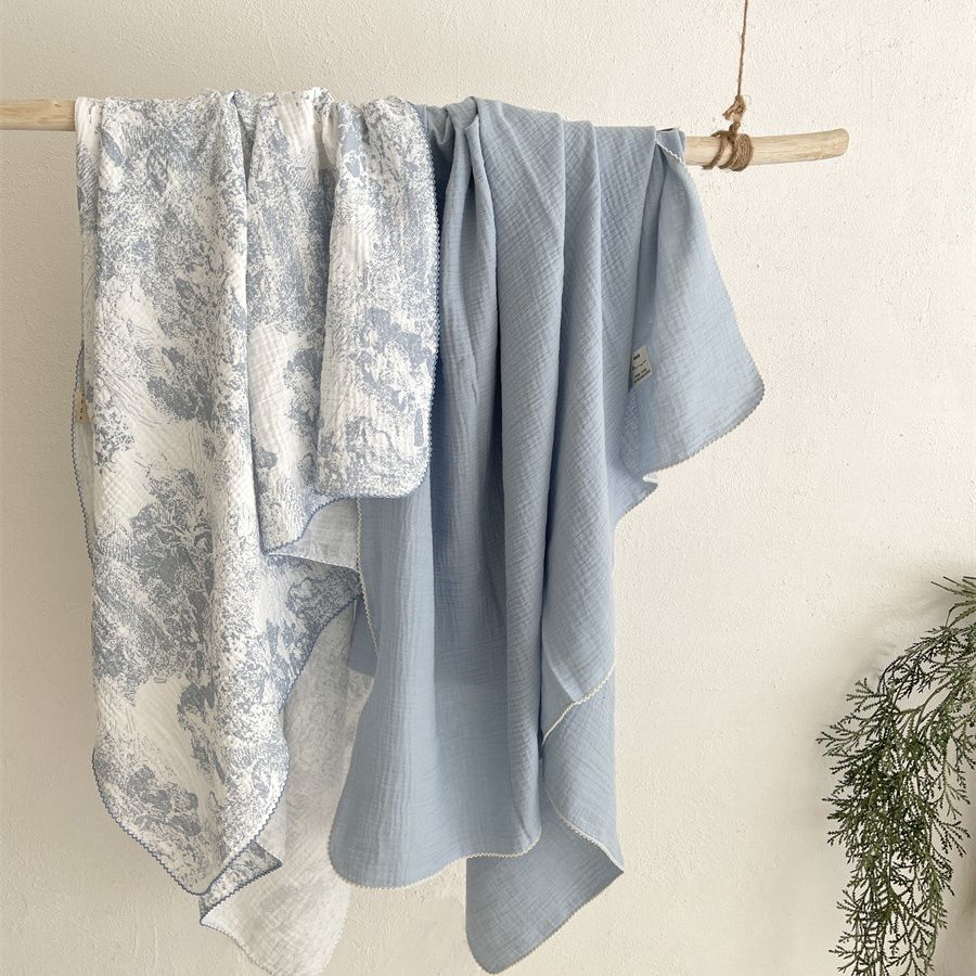 A light blue muslin swaddle blanket with a floral print is hanging on a wooden rack.
