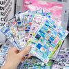A hand holds a colorful sticker pack featuring 27 unique designs for journals and crafts.