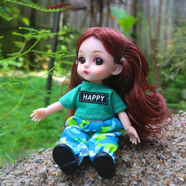 A 16cm articulated BJD princess doll with red hair wearing a green top and blue patterned pants sitting on a rock.