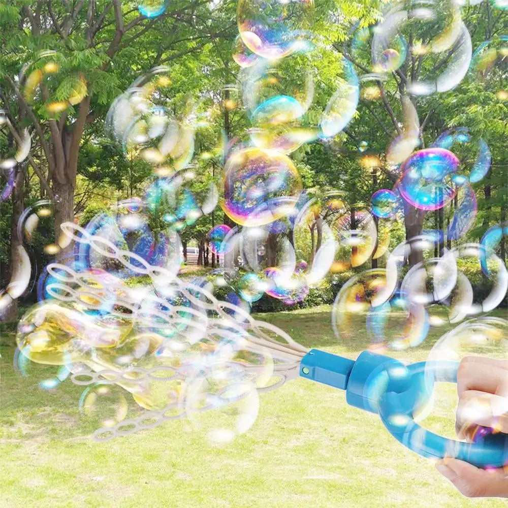 A hand holds a blue bubble wand creating numerous iridescent soap bubbles in an outdoor park setting.