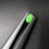 A bright green luminous fishing bead is shown resting on the serrated edge of a dark gray tool.