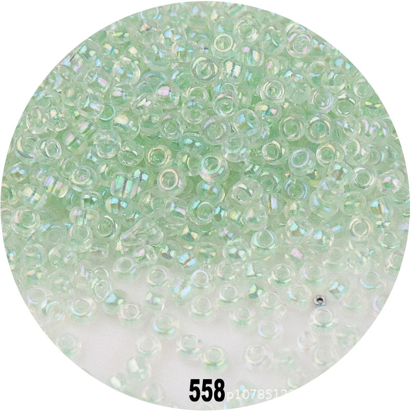 A circular image showing numerous small, round, colorful glass seed beads in various shades of green and clear.