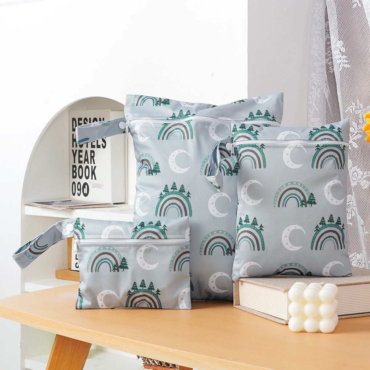 A set of three light blue waterproof wet and dry bags with green rainbow designs resting on a wooden table.