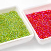 Two white dishes filled with green and red glossy glass seed beads for jewelry making