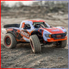 An orange and white high-speed 4WD brushless RC monster truck parked on a dirt surface.