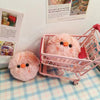 A pink squeaky plush pig keychain is displayed inside a pink plastic shopping basket on a light blue checkered surface.