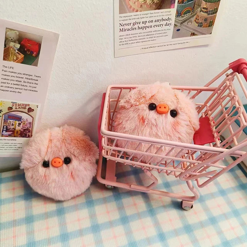 A pink squeaky plush pig keychain is displayed inside a pink plastic shopping basket on a light blue checkered surface.
