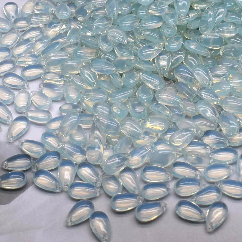 Clear blue water drop glass beads scattered on a white surface for jewelry making