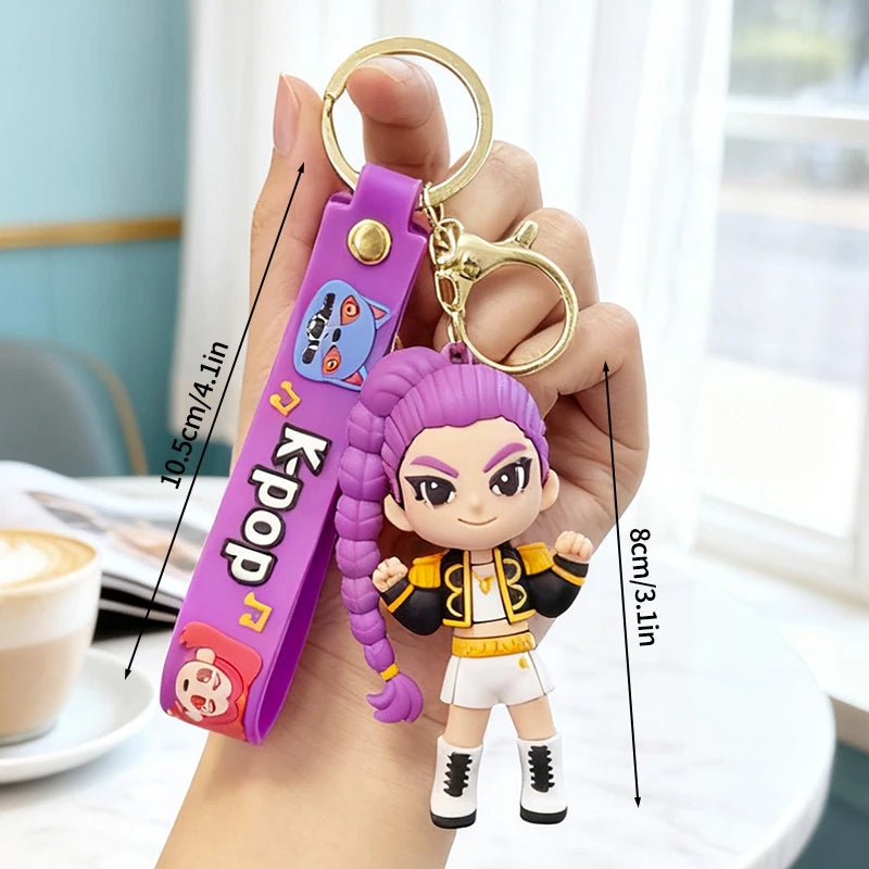 A hand holds a purple Kpop Rumi keychain charm featuring a stylized figure and a gold split ring.