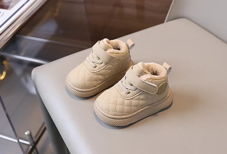 A pair of beige quilted toddler winter snow boots with soft soles and Velcro closures resting on a light surface.