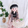A pink princess doll wearing a black and white striped outfit and a black hat, posed next to a potted plant.