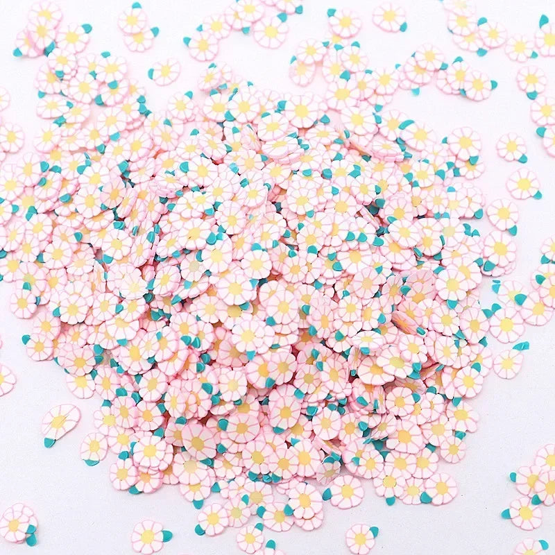 A pile of small polymer clay flower charms in pink and yellow colors scattered on a white surface.