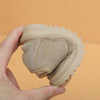 A hand holds a tan cozy leather winter boot for toddlers with an anti-slip rubber sole.