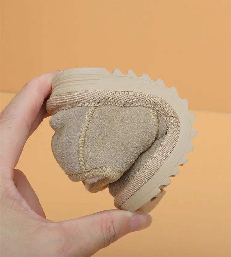 A hand holds a tan cozy leather winter boot for toddlers with an anti-slip rubber sole.