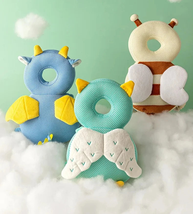 Three soft fabric head protectors shaped like animals in blue, yellow, and green floating on white clouds.