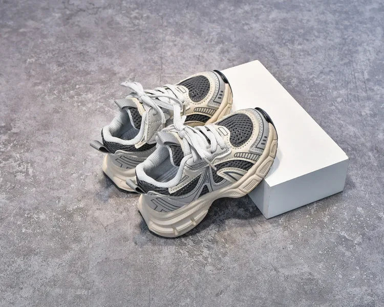 A pair of gray and white breathable mesh kids running sneakers resting on a white box.