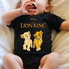 A baby wearing a black Lion King themed bodysuit is lying down on white bedding.