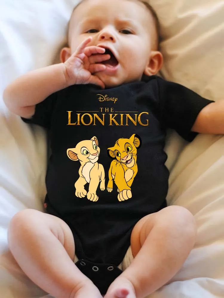 A baby wearing a black Lion King themed bodysuit is lying down on white bedding.