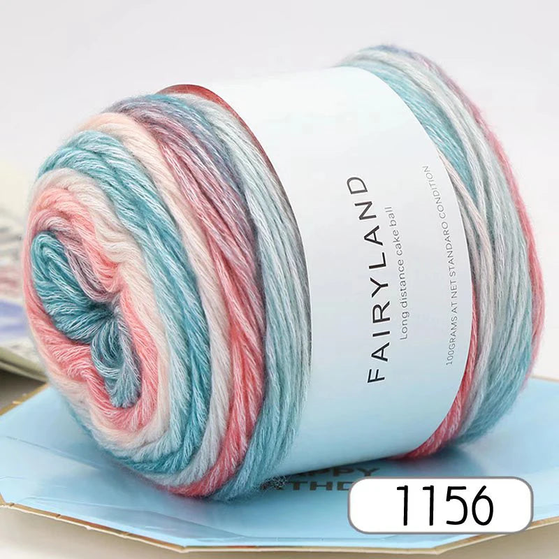 A spool of gradient rainbow yarn with pink, blue, and red strands resting on a light blue surface.